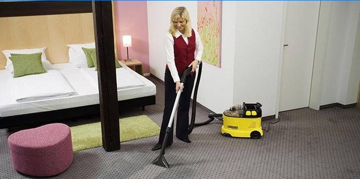 Jenta rengjør teppet med en støvsuger
