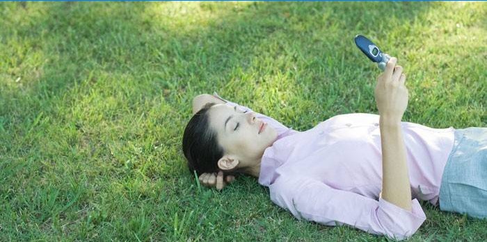 Jenta ligger på gresset med en telefon