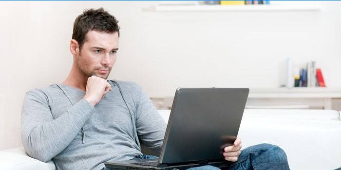 En mann sitter i en sofa med en bærbar datamaskin