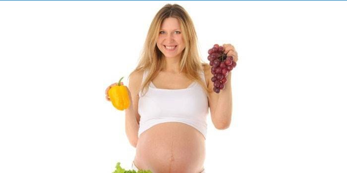 En gravid kvinne holder pepper og en haug med druer i hendene