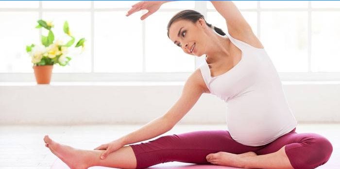 Gravid kvinne utfører en øvelse mens hun sitter på gulvet