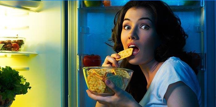 Jente som spiser kjeks foran et åpent kjøleskap