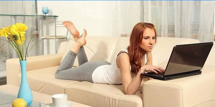 Jenta ligger på en sofa med en bærbar datamaskin